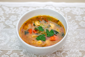 Sopa de legumes e frango em porcelana branca sobre toalha de mesa branca de renda.