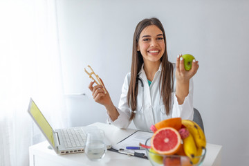 Young female nutritionist sitting at table with fresh vegetables and fruits in her office. Female nutritionist sitting at table with clipboard and healthy products on white background - obrazy, fototapety, plakaty