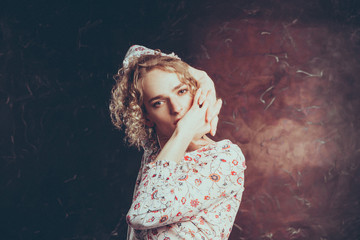 Fototapeta premium A young blond handsome man androgyn in the image of an attractive woman posing covering his mouth with his hands on a dark background.