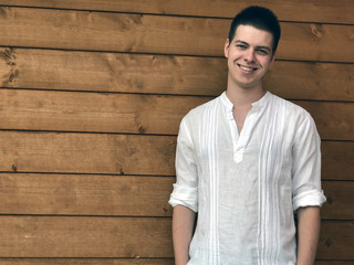 portrait of a young man in white shirt smiling across wooden background. Copy space