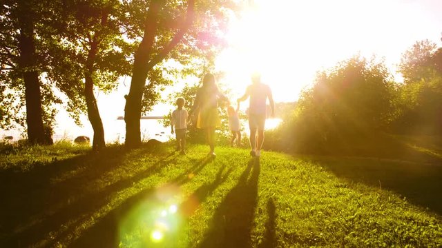 Happy family walking near the sea. Field and trees in countryside. Warm colors of sunset or sunrise. Loving parents and beautiful children. Love and parenthood.