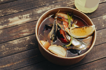 Fresh hot fish soup with ingredients and spices for cooking on wooden background. Street food