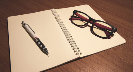 Fototapeta premium notebook with pen and glasses on wooden table.