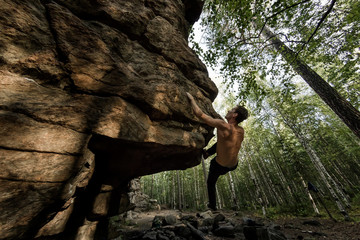 Rock climber climbs bouldering on a cliff on forest. Low angle of strong rock climbing man hanging free on rock with sunflare