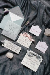 Flat lay wedding invitation, calligraphy and close-up cards with ribbons, marble stones on grey textile background