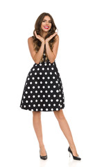 Beautiful Young Woman In Black Cocktail Dress In Polka Dots Is Holding Head In Hands And Smiling