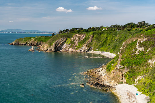 View from the popular hiking coastal trail Howth Cliff Walk in county Dublin, Ireland on a sunny summer day with blue Irish Sea clear waters and stunning wild beaches and green cliffs.