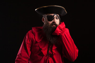 Attractive bearded man in a pirate costume for carnival touching his eye patch with his arm hook