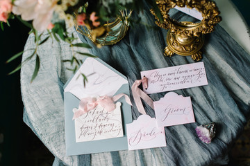 Bridal table wedding bouquet, golden vintage mirror, calligraphy and close-up cards with ribbons, marble stones on grey textile background