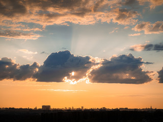 Buildings silhouettes over forest on sunset twilight and orange tone sky with long clouds as background in evening haze with rays from sun behind clouds. Sunny weather (Moscow city, Russia)
