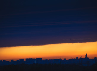 Dark cloudscape on sunset with stripe of the clear sky, over the panoramic silhouette of the buildings. Moscow city skyline, evening urban landscape.