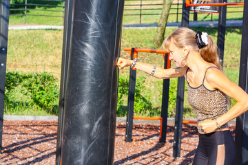 Obraz premium Woman boxer boxing a punching bag outdoors, doing workout. Athletic girl in sportswear training, standing in boxing position with fists