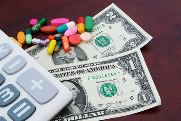 US dollars, calculator and drugs on brown  wooden table, cost of medicine concept