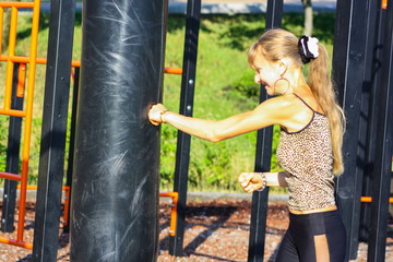 Obraz premium Woman boxer boxing a punching bag outdoors, doing workout. Athletic girl in sportswear training, standing in boxing position with fists