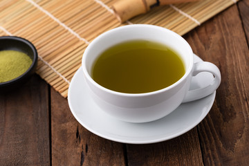 Hot green tea in cup on wood