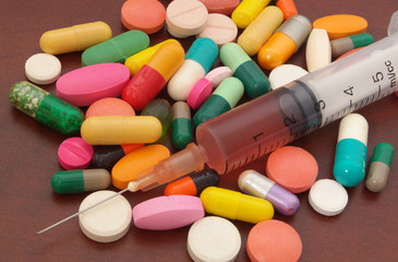 Colorful drugs, pills and syringe on wooden table close up, pharmacy and medical concept.