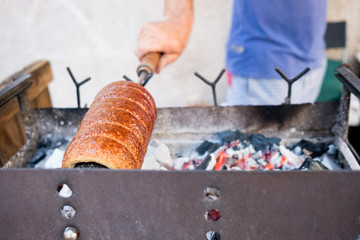 close up of man cooking and baking  sweet romanian horn bread known as Kürtös kalács in outdoor street food market
