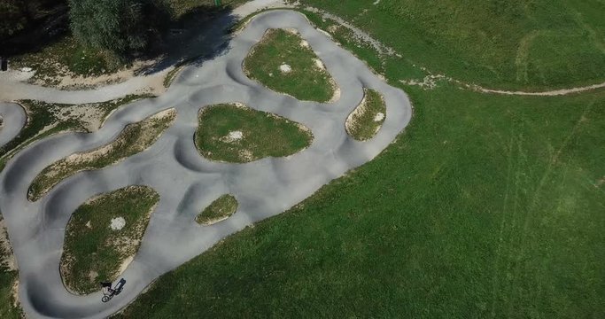 AERIAL 4K: Sport activity. Competitive athletic young bmx rider carving berms and pumping for speed at the urban concrete skate park pump track. Camera top down, circling subject.