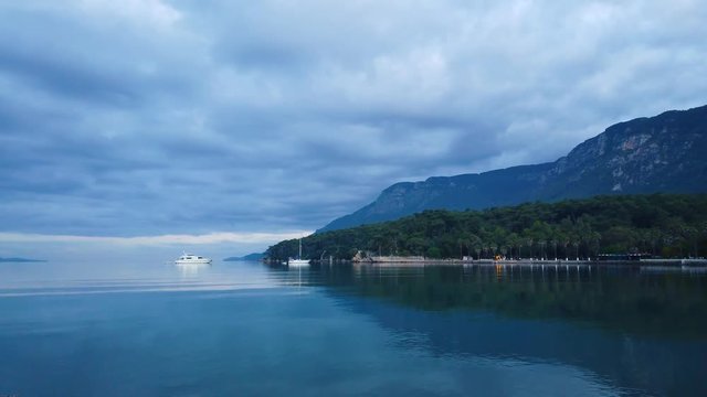 Partial view of Akyaka shoreline (Gulf of Gokova, Aegean Sea) on a cloudy spring morning. The calm sea reflects the coastline like a mirror. Shot and presented at 60 fps.