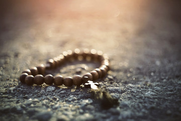 Forgotten lost wooden rosary with a cross lying on the pavement, illuminated by sunlight. Sunlight is presented here as a sacred illumination of God's light