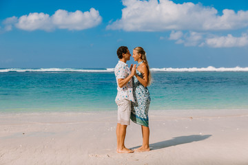 Beautiful pregnant woman with husband expecting baby at tropical beach with blue ocean