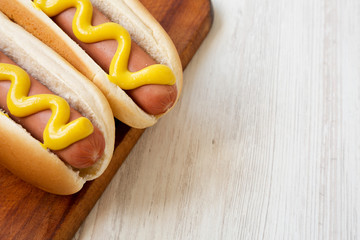 Hotdog with yellow mustard on a rustic wooden board on a white wooden surface, low angle view. Copy...