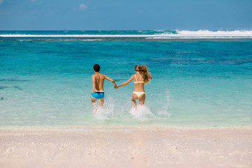 Naklejka premium Happy running couple. Pregnant woman with husband expecting baby at tropical beach with blue ocean