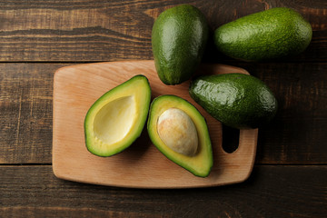 Fresh ripe tasty avocado on a cutting board on a brown wooden background. tropical fruit top view.