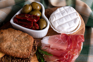 still life crispy pizza, prosciutto, cheese ,green olives, dried tomatoes on a wooden plate.