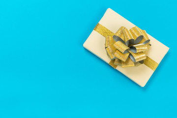 beautiful gift box wrapped in paper with a gold ribbon and a bow on a blue surface. Top view