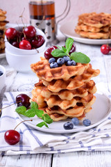 Stack of waffles topped with fresh bilberries, cherries and mint on the white wooden table
