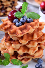 Stack of waffles topped with fresh bilberries, cherries and mint on the white wooden table