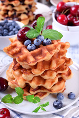 Stack of waffles topped with fresh bilberries, cherries and mint on the white wooden table