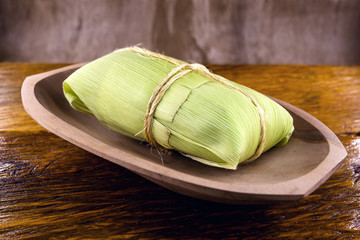 Fototapeta na wymiar pamonha-Brazilian typical of rural towns. Sweet corn with cheese served in straw. Concept of rural and regional Brazilian food.