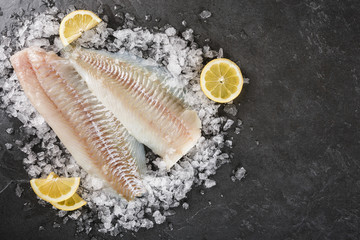 Fresh raw fillet white fish Pangasius with spices on ice over dark stone background.  Seafood, top view, flat lay, copy space - obrazy, fototapety, plakaty
