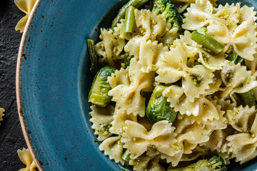 Vegan Farfalle pasta in a spinach sauce with broccoli, brussels sprouts, green beans in plate on dark stone background. Top view, Flat lay. Vegetarian food