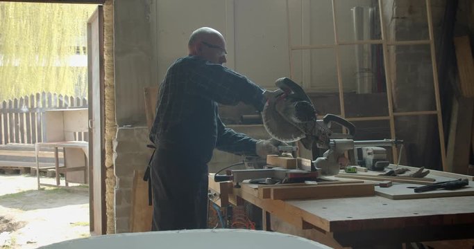 Portrait of male caucasian carpenter carving the wood with headsaw in manufacture.