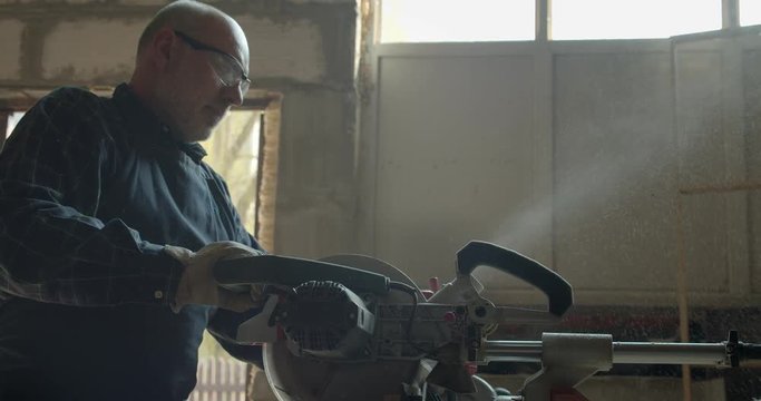 Portrait of male caucasian carpenter cutting the wood with headsaw in manufacture.