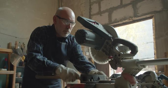 Senior male master working at wood factory with headsaw and ruler being concentrated and serious.