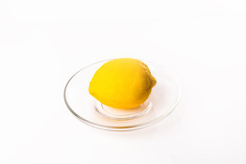 Yellow lemon on transparent glass plate on white background. Lemon to tea cut into smooth slices.
