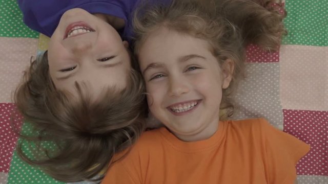 Friends selfie. Excited young children playing lying on the bed and taking a selfie. Little brother and sister monkeying on camera and kissing. Family taking a selfie with a smartphone. Close up.