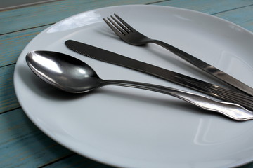 In a white plate are cutlery knife, fork, spoon