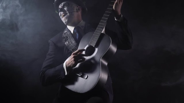Santa Muerte carnival, a man in black suit is playing a black and white guitar