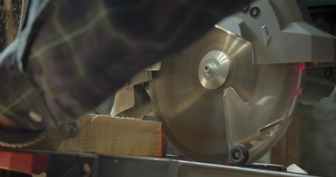 Close-up shot of hands of male senior carpenter carving the wood with headsaw into small squares at manufacture.