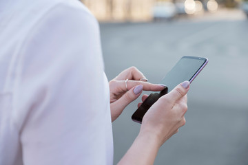 Beautiful brunette business woman in white skirt and grey suit trousers working on a mobile phone in her hands outdoors. European city on background. copy space