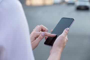 Beautiful brunette business woman in white skirt and grey suit trousers working on a mobile phone in her hands outdoors. European city on background. copy space