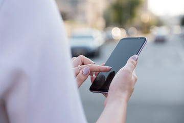Beautiful brunette business woman in white skirt and grey suit trousers working on a mobile phone in her hands outdoors. European city on background. copy space