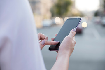 Beautiful brunette business woman in white skirt and grey suit trousers working on a mobile phone in her hands outdoors. European city on background. copy space