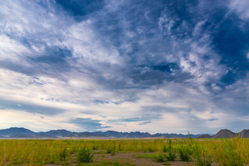 panoramic view of plain at root of mountains with white fluffy clouds in blue sky 