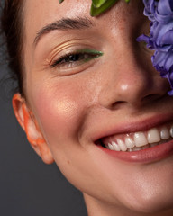 Pretty brunette woman with red creative make up and blue hyacinth flower near her face. Close up beauty concept with studio lighting